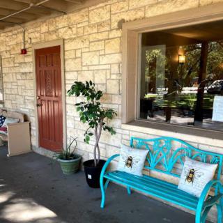 A cozy porch features a turquoise bench with decorative pillows, next to potted plants and a stone wall.