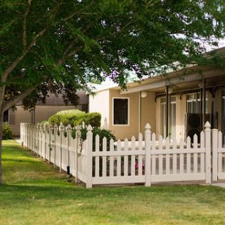 A cozy house with a white picket fence surrounded by lush greenery.
