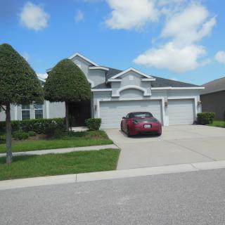 A suburban house with a car parked in the driveway under a partly cloudy sky.