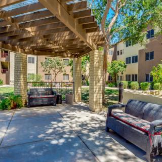 A shaded outdoor seating area with patio furniture under a pergola in an apartment complex garden.