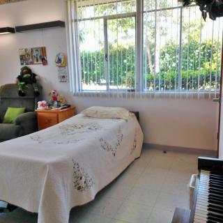 A cozy bedroom with a bed and piano near large windows.