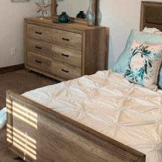 A cozy bedroom with a wooden bed and dresser, decorated with elegant bedding and pillows.