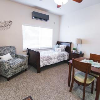 A cozy bedroom with a bed, armchair, and dining table set near a window.