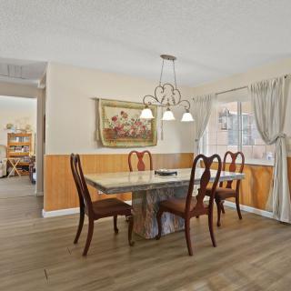 A cozy dining room with a wooden table and chairs, enhanced by a chandelier and curtains.
