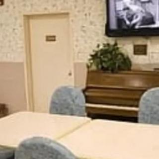 A room with tables, chairs, a piano, and a television mounted on the wall.