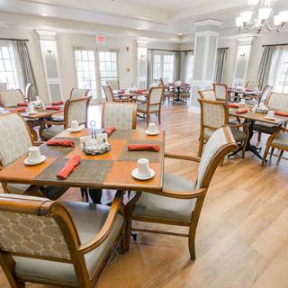 An elegantly set dining room with multiple tables and chairs on a wooden floor.