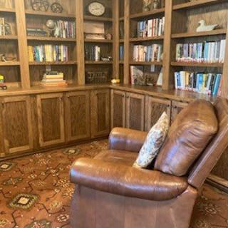 A cozy library with a leather chair and wooden bookshelves filled with books.
