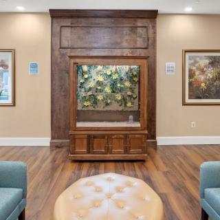 A cozy waiting room featuring an aquarium set within a wooden paneled wall, surrounded by artwork and comfortable seating.