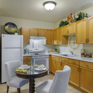 A cozy kitchen with wooden cabinets, white appliances, and a small dining table set for two.