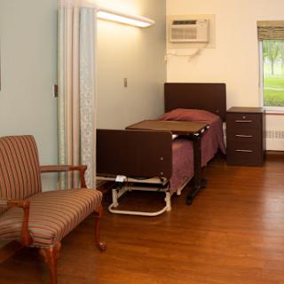 A simple hospital room featuring a bed, chair, and basic furnishings.