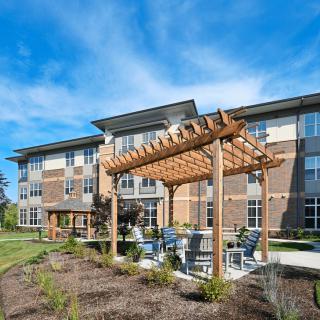 A modern apartment building with a wooden pergola and outdoor seating area under a clear blue sky.