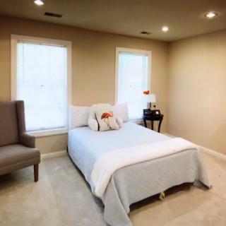 A cozy and minimalist bedroom featuring a comfortable bed, armchair, and two large windows.