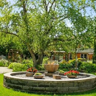 A serene garden featuring a circular stone fountain surrounded by lush greenery and colorful flowers.