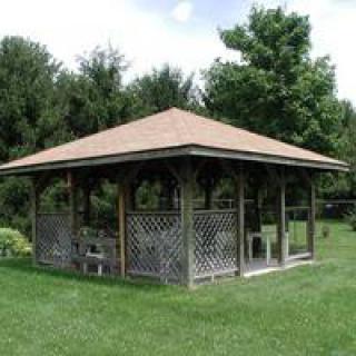 A wooden gazebo with a lattice design in a garden setting.