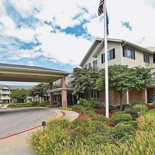 A large building with a covered entrance and an American flag, surrounded by well-maintained landscaping under a partly cloudy sky.