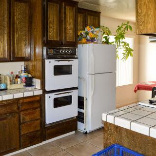 A cozy kitchen with wooden cabinets, a double oven, and a white refrigerator adorned with plants on top.
