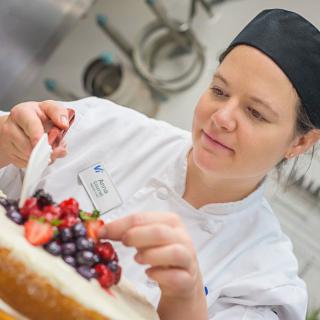 A chef decorating a cake with fresh fruits in a kitchen.