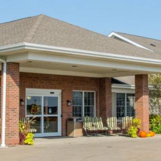 The image shows the entrance of a brick building with large windows and a covered porch.