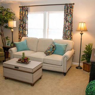 A cozy living room with a beige sofa, decorative pillows, and a coffee table, accented by lamps and potted plants.