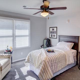 A cozy bedroom with a single bed, ceiling fan, and natural light streaming through blinds.
