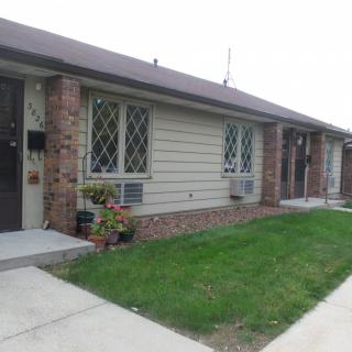 A row of single-story residential houses with brick facades, featuring lawns and concrete pathways.