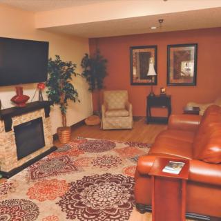 A cozy living room with a leather sofa, patterned rug, and a wall-mounted TV above the fireplace.