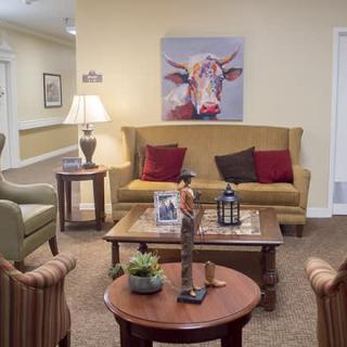 A cozy living room featuring a sofa, various chairs, and a coffee table adorned with decorative items. A colorful cow painting hangs on the wall, adding a playful touch to the space.