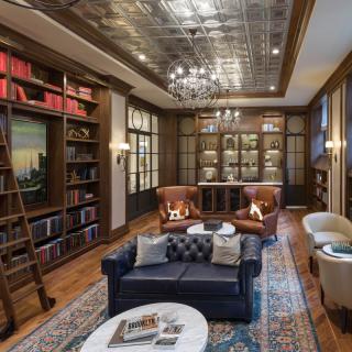 A luxurious library with leather armchairs, a sofa, and extensive bookshelves under a decorative ceiling.