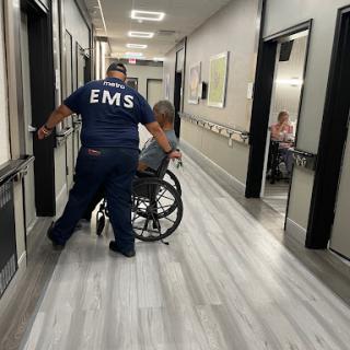 An EMS worker assisting a patient in a wheelchair along a hospital corridor.