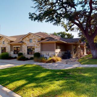 A beautiful stone house with well-maintained landscaping and a large tree in the front yard.