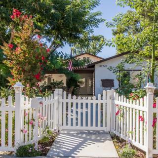 A charming house with a white picket fence, surrounded by lush trees and vibrant flowers.