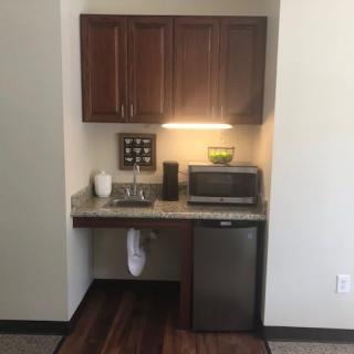 A small kitchenette area with cabinets, sink, refrigerator, and microwave.
