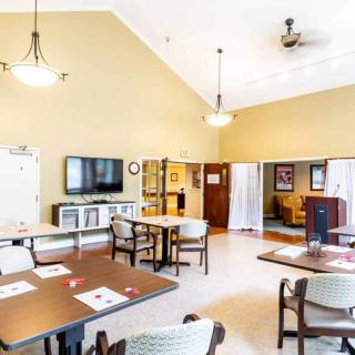 A bright and airy dining room featuring several tables and chairs, a television, and warm lighting.