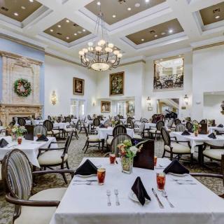 An elegant restaurant dining room with formal table settings and chandeliers.
