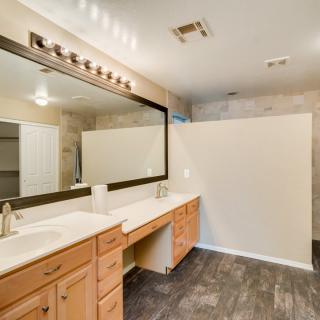 A modern bathroom featuring a double vanity with wooden cabinets and large mirror, accented by overhead lighting and tile flooring.