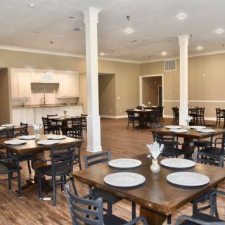 A well-arranged dining room with multiple tables set for dining, featuring elegant decor and wood flooring.
