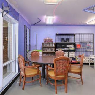 A cozy and inviting room designed for reading and gatherings, featuring a round table surrounded by wicker chairs against a soft purple backdrop.