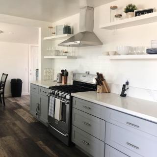 A modern kitchen with white cabinetry, stainless steel appliances, and open shelving.