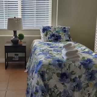 A cozy bedroom with a single bed adorned in blue floral bedding, illuminated by natural light through the window.