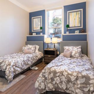 A cozy bedroom featuring twin beds with floral bedding, complemented by elegant wall art and a centrally placed nightstand with lamps.