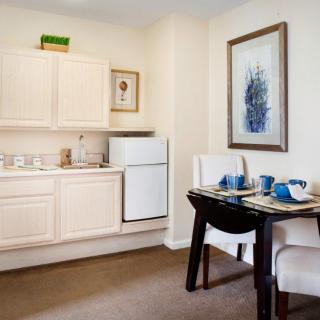 A cozy kitchen and dining area with a small table set for two, featuring white cabinetry and a refrigerator.