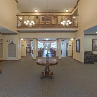 A spacious lobby area featuring chandeliers, a central table, and an upper balcony.