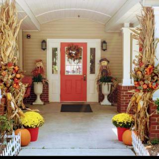 A beautifully decorated front porch with autumn-themed decor including pumpkins, mums, and a festive wreath.