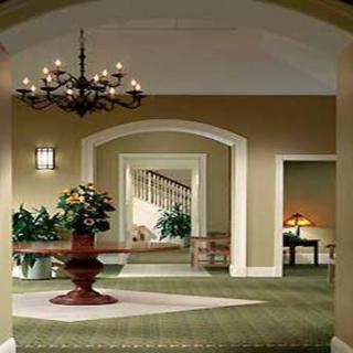 A beautifully decorated hallway featuring a central table with plants, elegant chandeliers, and an inviting staircase.