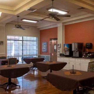 A cozy dining area with several tables and chairs, featuring a beverage station against the wall and large windows letting in natural light.