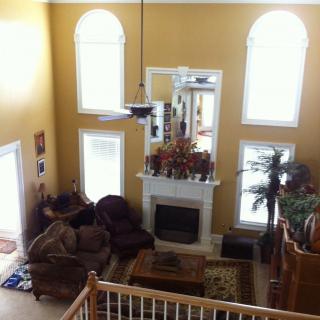 A spacious living room with a high ceiling, featuring large windows, a fireplace, and comfortable seating.