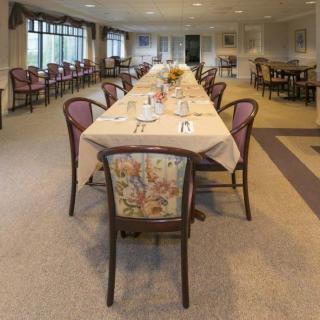 An elegantly set dining room with a long table and upholstered chairs, ready for guests.
