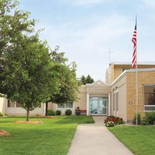 A school building with an American flag and surrounding greenery.