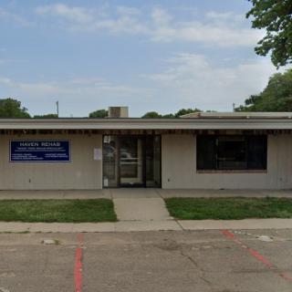 A small office building with a parking lot and surrounding trees under a partly cloudy sky.