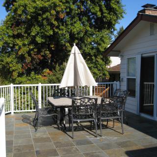A sunny patio with outdoor furniture and an umbrella, surrounded by trees.